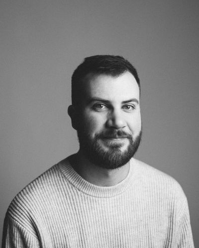 Black and white portrait of Justin Delorme, a man with a beard wearing a textured sweater.